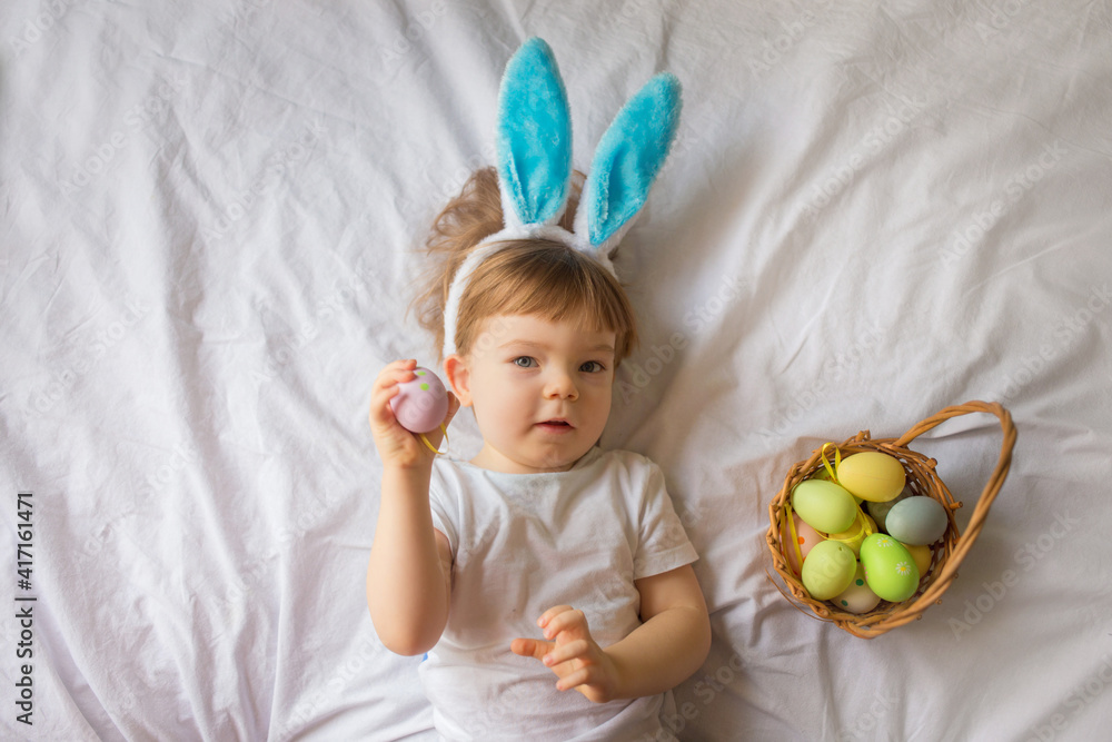 Cute funny baby with bunny ears and colorful Easter eggs at home on a white background Cute funny baby with bunny ears and colorful Easter eggs at home on a white background