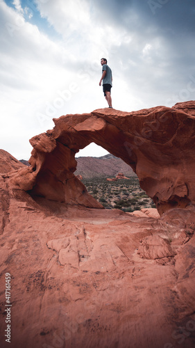 A guy standing on a arches in the valley of fire state park, USA