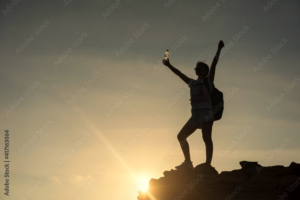 Silhouette hiker woman raise hands to celebrate after climbing to mountain summit at sunset. Extreme outdoor adventure sport. Bodybuilding and Healthy lifestyle.