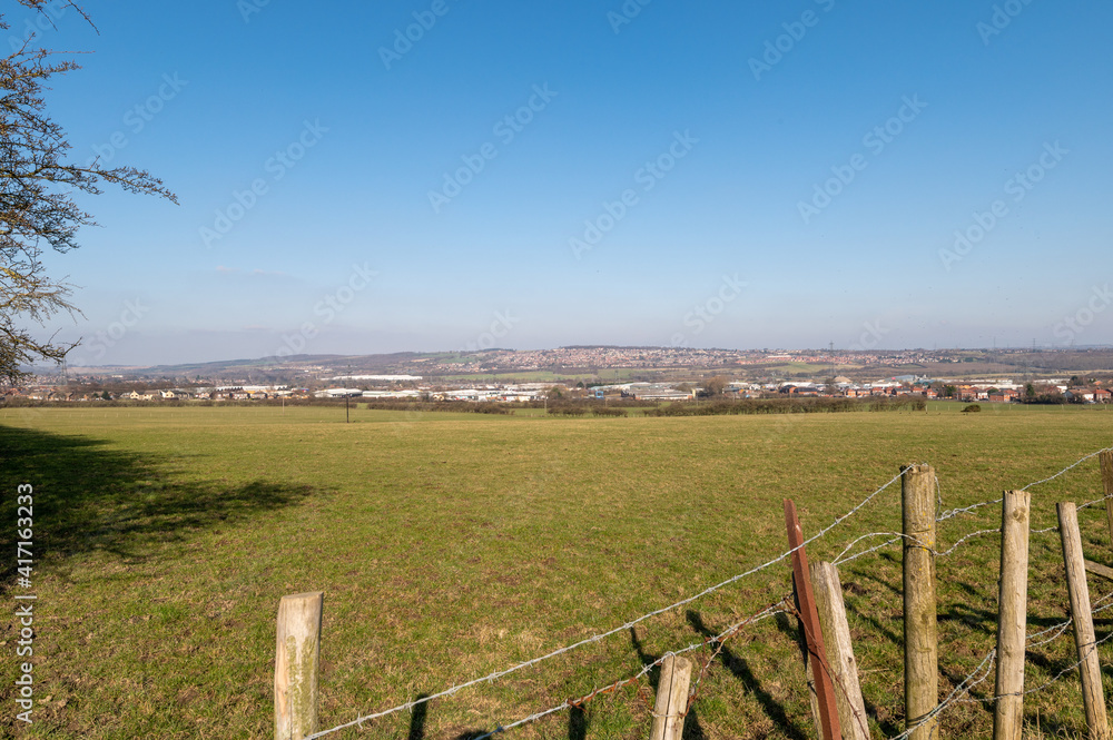 Looking across a barbed wire fence and a farmers field towards the town of Barnsley