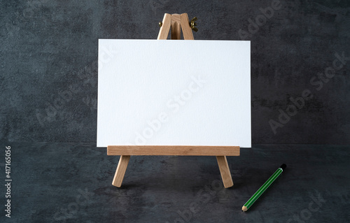 wooden easel with white board with space for text and green pencil on gray background