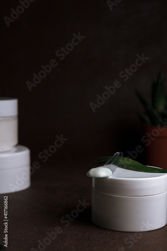 Facial cream in jar and on spatula arranged on dark background in studio for skin care and beauty routine concept 