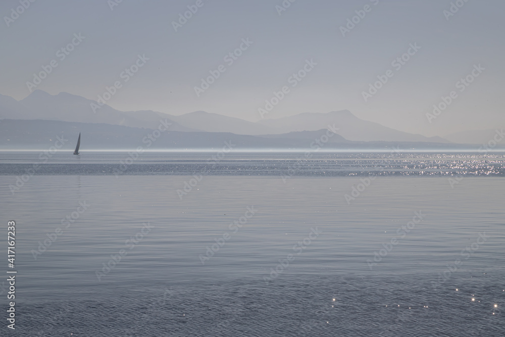 A boat on hazy, misty Lake Geneva and the Alps seen from Lausanne, Switzerland A boat on hazy, misty Lake Geneva and the Alps seen from Lausanne, Switzerland