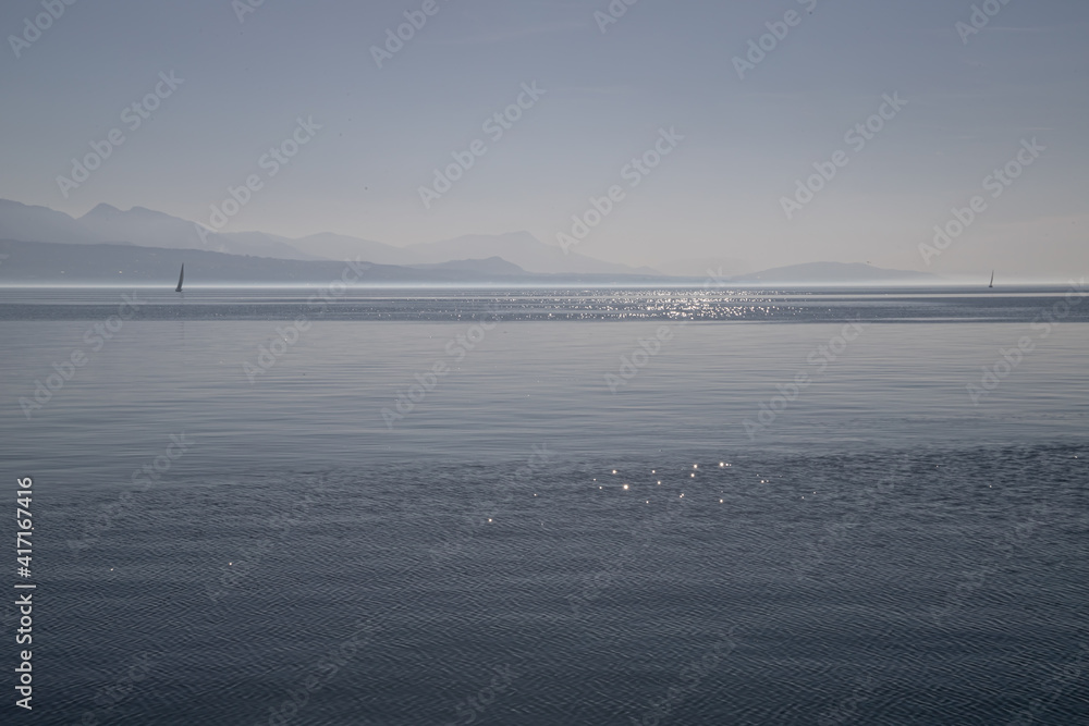 A boat on hazy, misty Lake Geneva and the Alps seen from Lausanne, Switzerland
