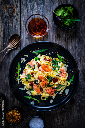 Tagliatelle with salmon nuggets, arugula and sun-dried tomatoes on wooden table
