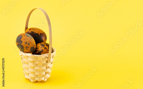 Easter quail eggs in a basket on yellow background. Easter holiday concept. Copy space, close up