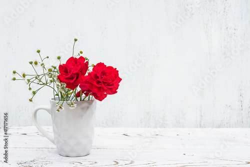 Fototapeta Naklejka Na Ścianę i Meble -  Red roses in white mug on white paint wooden background. Space for text