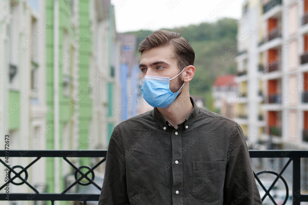 Young handsome man in medical protective mask stands near colorful buildings