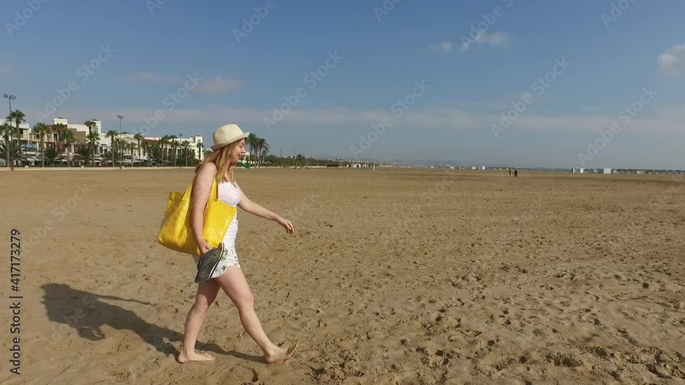 A beautiful girl walks on a sandy beach in Valencia, Spain. Happy Young woman in shorts, T-shirt and hat with yellow bag. High quality FullHD footage A beautiful girl walks on a sandy beach in Valencia, Spain. Happy Young woman in shorts, T-shirt and hat with yellow bag. High quality FullHD footage