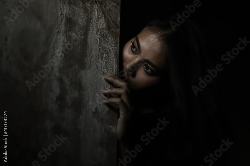 Scared woman hiding behind wall in dark room Young crazy scared and shocked asian woman escape murderer and get frightened Copy space Facial expression, human emotion concept Looking horror Halloween