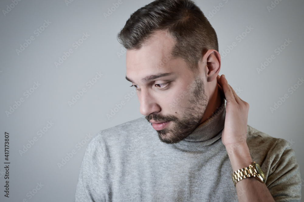 Portrait of a young man with a short beard that looks embarrassed in conversation and touches his neck Portrait of a young man with a short beard that looks embarrassed in conversation and touches his neck