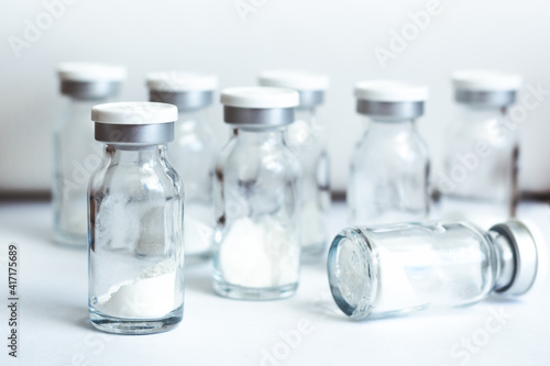 Glass sealed vials with medicine in powder form on light background, selective focus