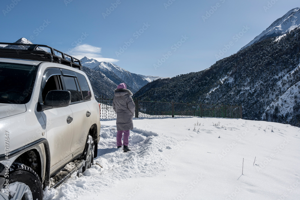 woman in gray jacket and sunglasses in the snow-capped mountains of the Caucasus woman in gray jacket and sunglasses in the snow-capped mountains of the Caucasus