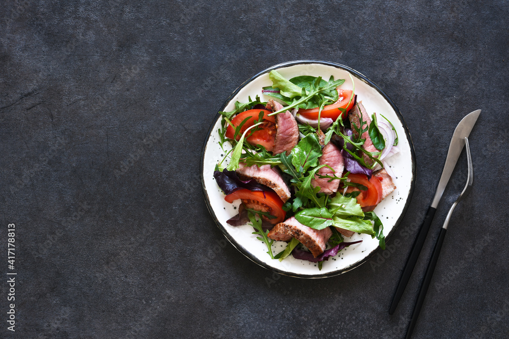 Mix salad with tomatoes and medium beef in a plate on a dark background. Mix salad with tomatoes and medium beef in a plate on a dark background.