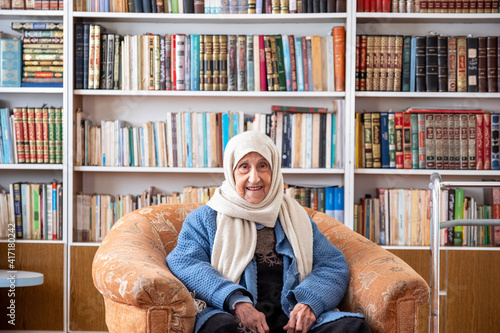 Arabic old woman sitting on couch in her home with a library background