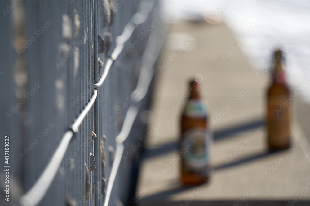 Fototapeta premium Gabion fence made of steel bars filled with gray granite stones. Park bench with beer bottles. Side view. Selective focus. Winter in Germany.