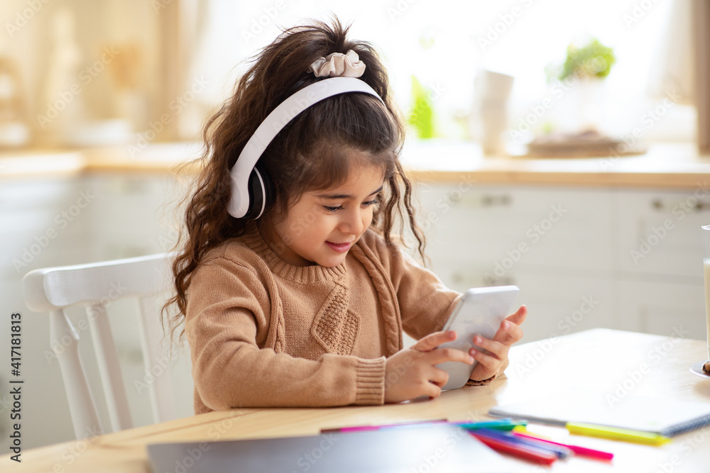 Kids And Gadgets. Cute Little Girl In Wireless Headphones Playing With Smartphone Kids And Gadgets. Cute Little Girl In Wireless Headphones Playing With Smartphone