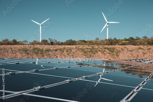 Solar panels under a beautiful blue sky reflecting windmills of an eolic windfarm. Renewable energy generation for environmental conservation concept.  photo