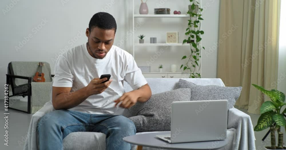 Afro american guy sleeping at home on couch on pillow waiting for call businessman freelancer wakes up from sound of mobile phone speaks on smartphone receives urgent information types data in laptop Afro american guy sleeping at home on couch on pillow waiting for call businessman freelancer wakes up from sound of mobile phone speaks on smartphone receives urgent information types data in laptop