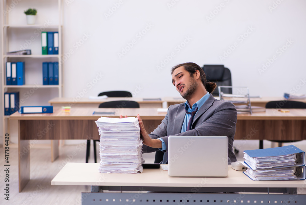 Young male employee unhappy with excessive work in the office Young male employee unhappy with excessive work in the office