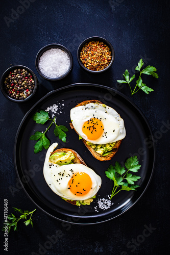 Continental breakfast - sunny side up eggs on toasted bread with avocado on black background 