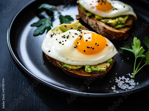 Continental breakfast - sunny side up eggs on toasted bread with avocado on black background
