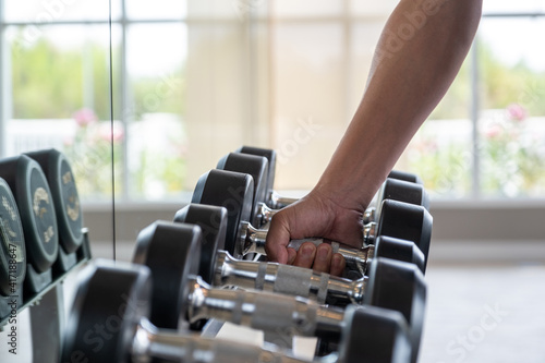 Close up man hand picking or choosing dumbbell from dumbbell racks at the gym.