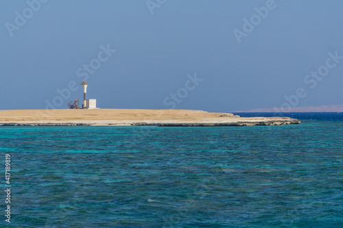 Lighthouse on sore with blue water and sand beach