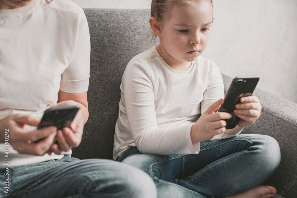 Mom and daughter are addicted to a smartphone. Harm of electronic devices for children. High quality photo Mom and daughter are addicted to a smartphone. Harm of electronic devices for children. High quality photo