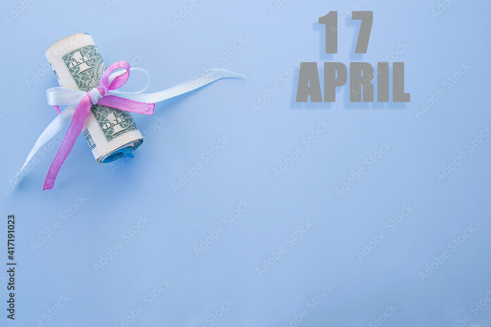calendar date on blue background with rolled up dollar bills pinned by blue and pink ribbon with copy space.  April 17 is the seventeenth day of the month