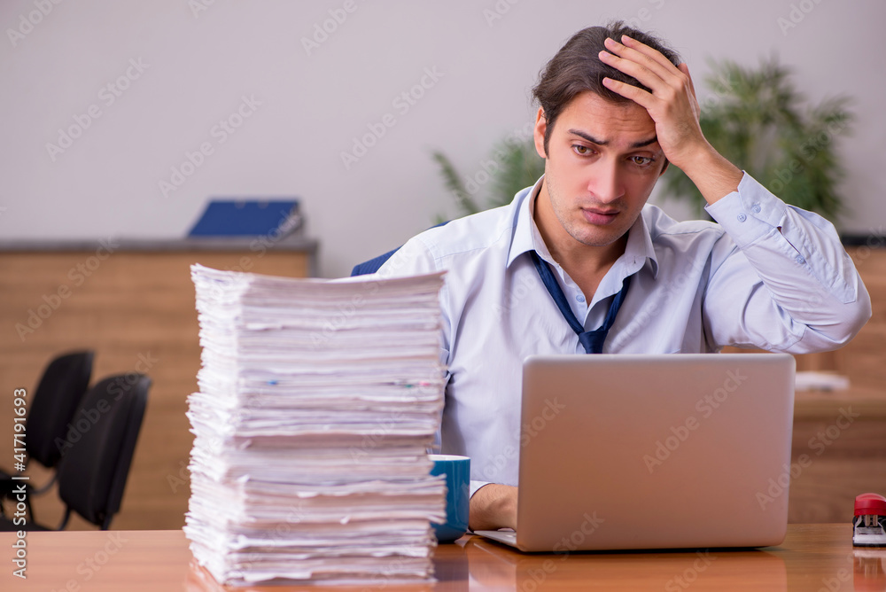 Young male employee unhappy with excessive work in the office Young male employee unhappy with excessive work in the office