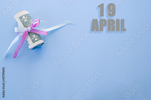 calendar date on blue background with rolled up dollar bills pinned by blue and pink ribbon with copy space. April 19 is the twenty-second day of the month