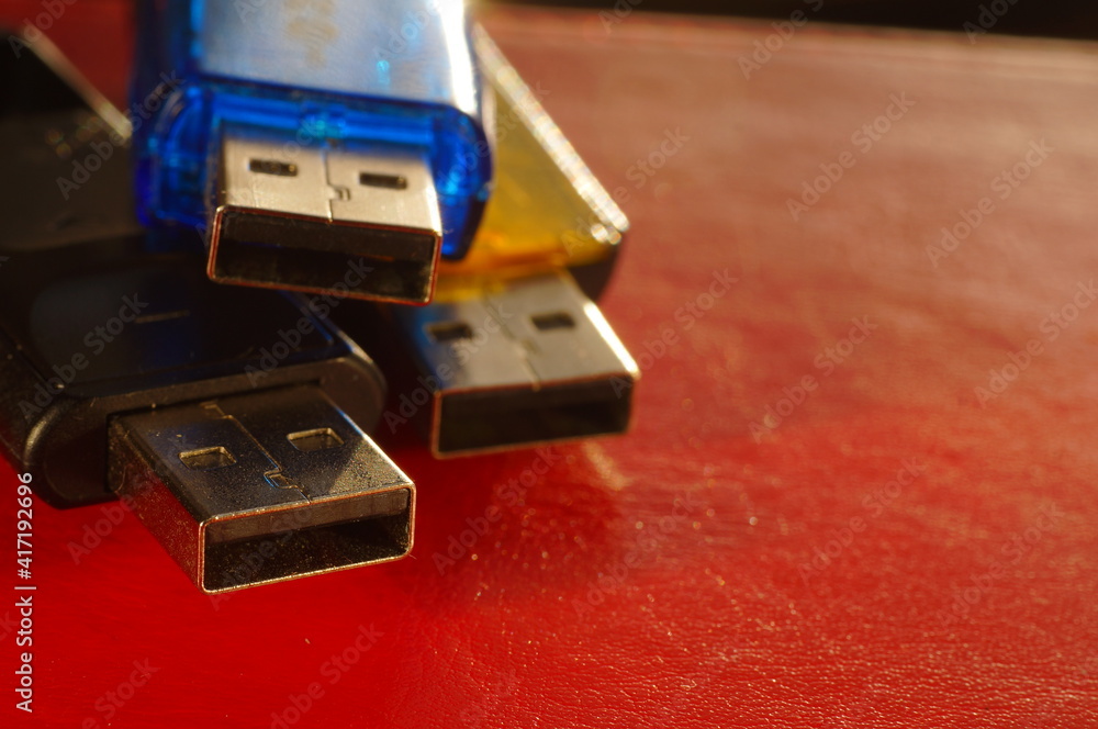 USB flash drive - black, yellow and blue, on a red background. Three used computer flash drives, ready to work. Close-up of a data memory stick, in several colors, on a bright background. USB flash drive - black, yellow and blue, on a red background. Three used computer flash drives, ready to work. Close-up of a data memory stick, in several colors, on a bright background.