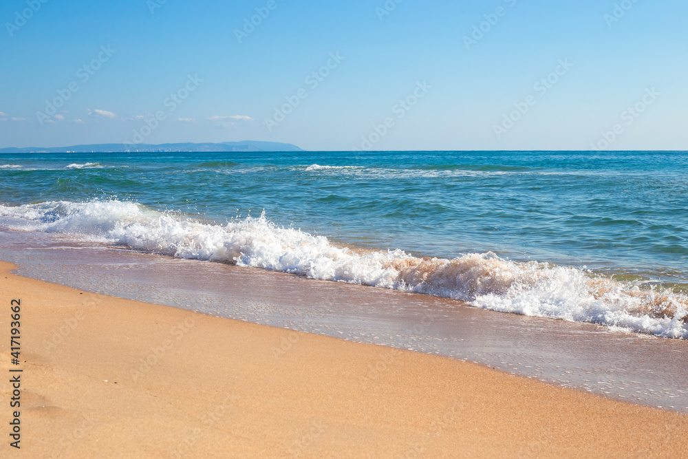 Sea coast on a sunny day. Wave with foam on the sandy shore. Travel and tourism.