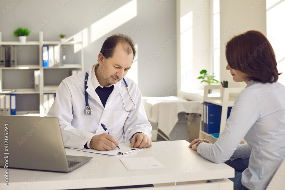 Healthcare in a hospital or private clinic. Middle-aged doctor writes a prescription to a female patient in his hospital office. Concept of disease prevention and consultations in the medical clinic. Healthcare in a hospital or private clinic. Middle-aged doctor writes a prescription to a female patient in his hospital office. Concept of disease prevention and consultations in the medical clinic.