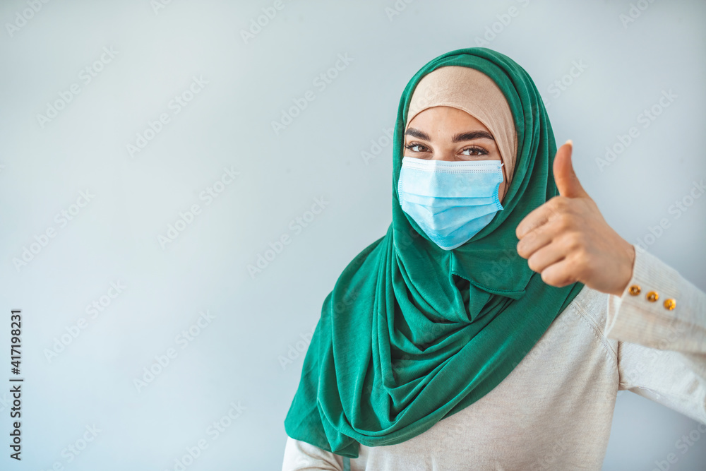 Beautiful Muslim young woman with disposable face mask. Protection versus viruses and infection. Studio portrait, concept with white background. Muslim Woman showing thumb up.