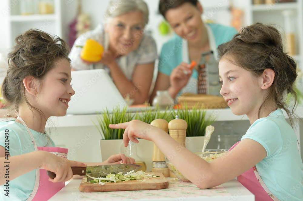 Cute girls preparing delicious fresh salad in kitchen, mother and grandmother