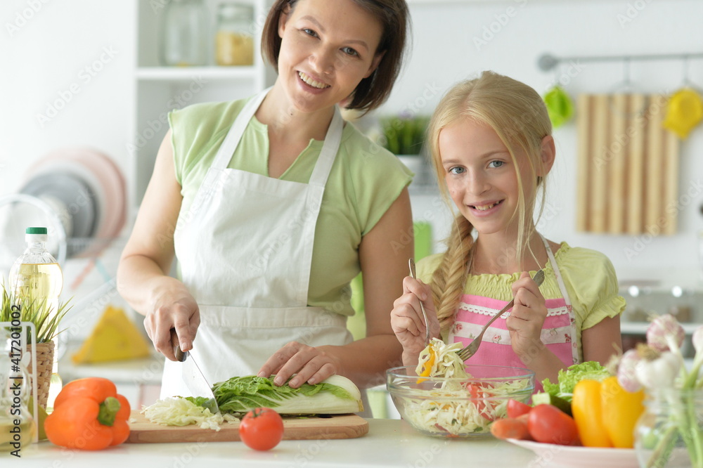 Cute little girl with her mother cooking together at kitchen table Cute little girl with her mother cooking together at kitchen table