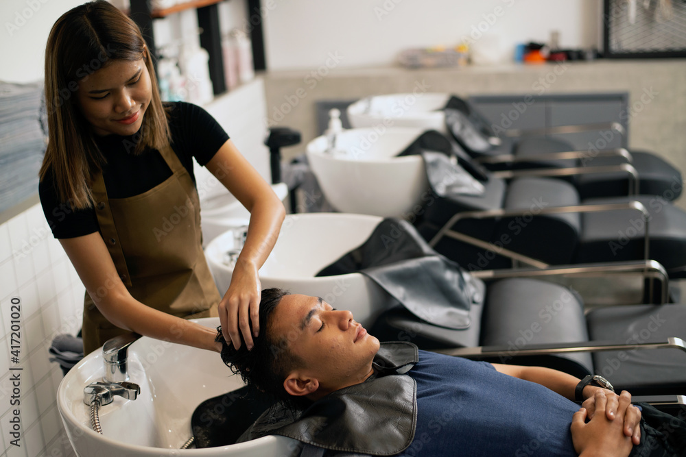A hairdresser washes hair for a customer in a barber shop the man lay on a chair in a robe . Which takes care of the hair and scalp professionally.. A hairdresser washes hair for a customer in a barber shop the man lay on a chair in a robe . Which takes care of the hair and scalp professionally..