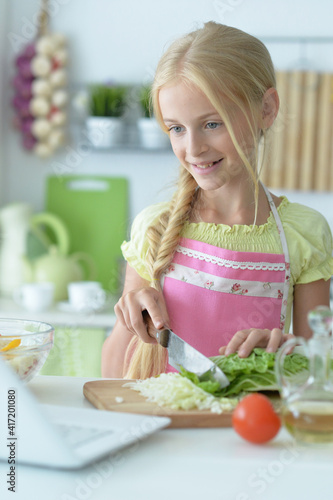 cute girl making salad on kitchen and using laptop