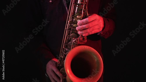 Close up of man playing vintage saxophone under red and blue lights, handheld dolly in