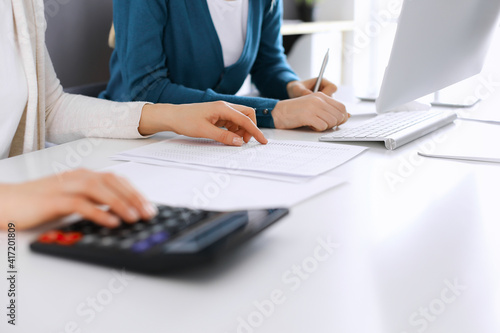 Accountant checking financial statement or counting by calculator income for tax form  hands close-up. Business woman sitting and working with colleague at the desk in office. Audit concept