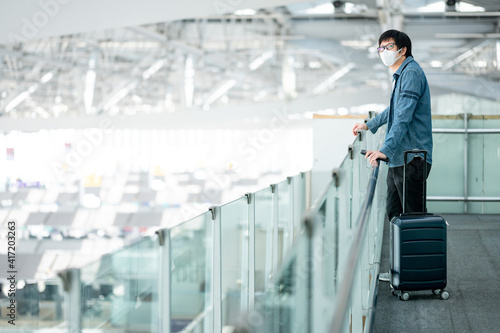 Asian man tourist with suitcase luggage wearing face mask waiting in airport terminal gate hall. Coronavirus (COVID-19) pandemic prevention when travel. Health awareness and social distancing