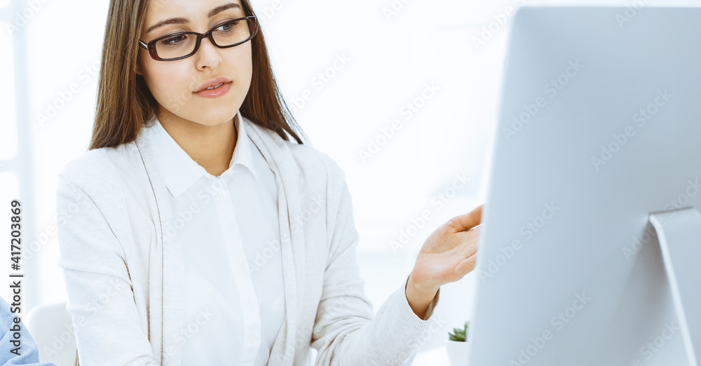 Young woman sitting at the desk with computer in white colored office. Looks like student girl or business lady communicating with casual dressed man Young woman sitting at the desk with computer in white colored office. Looks like student girl or business lady communicating with casual dressed man