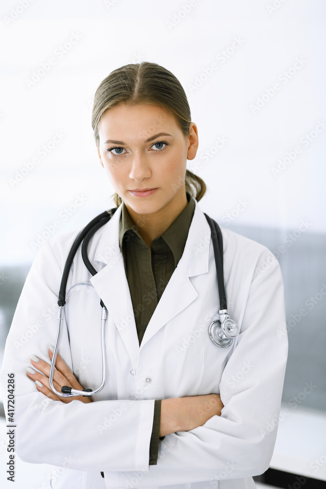 Woman-doctor standing with arms crossed and looking at camera. Perfect medical service in clinic. Medicine and healthcare Woman-doctor standing with arms crossed and looking at camera. Perfect medical service in clinic. Medicine and healthcare