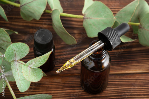 mockup glass bottle Essential oil or serum cosmetics with eucalyptus branches on wood brown background with copy space top view. Brown glass cosmetic bottle.