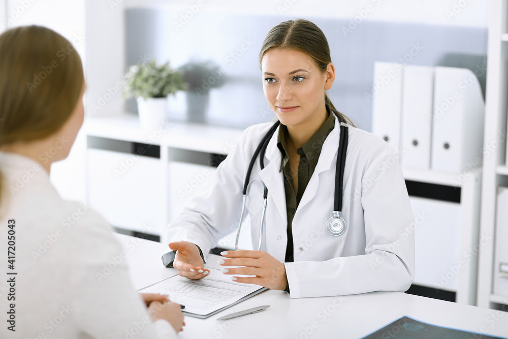 Woman-doctor and patient sitting and talking at hospital office. Green color blouse suits to therapist. Medicine and healthcare concept Woman-doctor and patient sitting and talking at hospital office. Green color blouse suits to therapist. Medicine and healthcare concept
