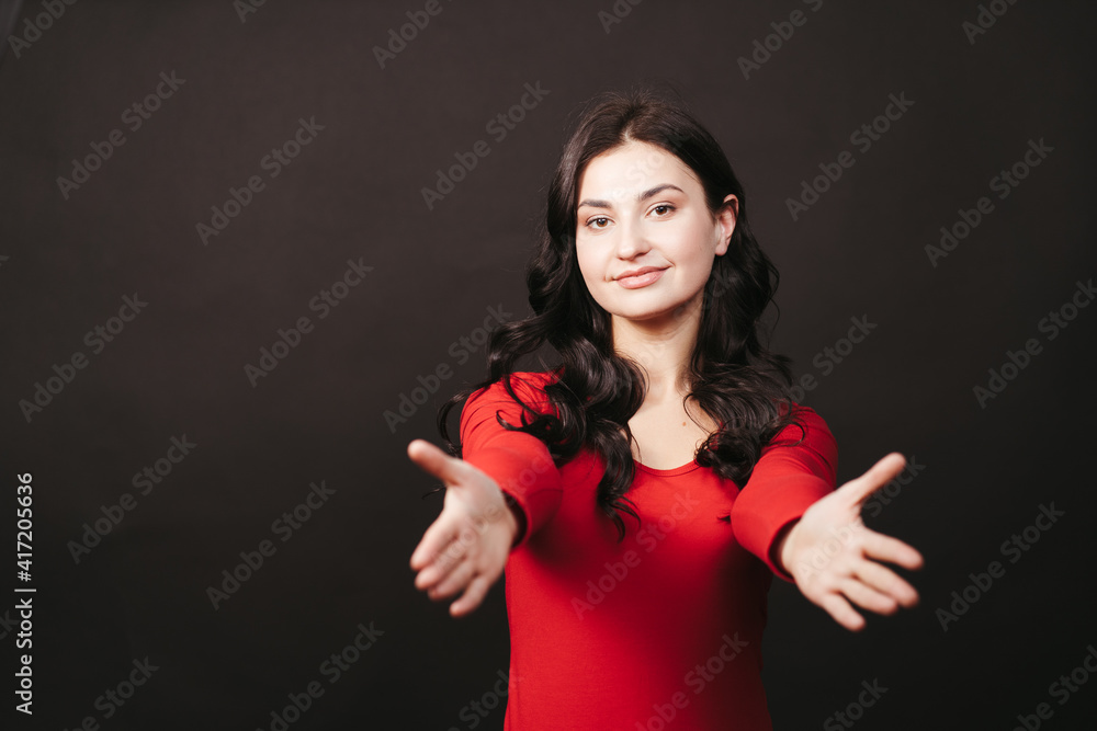Cute pretty curly-haired woman in red sweater stretching hands forward, smiling and gazing camera with love and care to give hug, cuddle friend. Friendly concept Cute pretty curly-haired woman in red sweater stretching hands forward, smiling and gazing camera with love and care to give hug, cuddle friend. Friendly concept