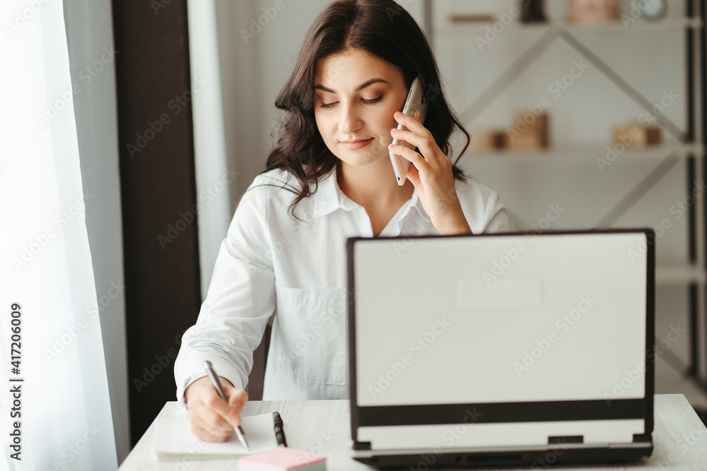 Young business woman multitasking working with laptop and documents and speaking by phone. Productivity. Cozy office workplace, people at work, e-learning concept Young business woman multitasking working with laptop and documents and speaking by phone. Productivity. Cozy office workplace, people at work, e-learning concept