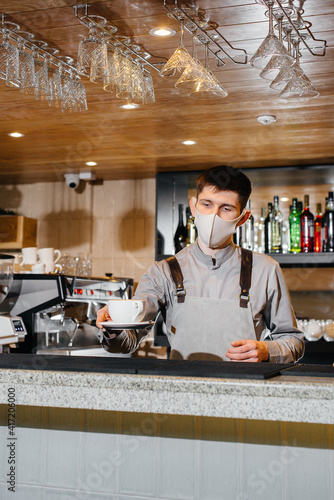 Submission of a Barista in a mask of delicious organic coffee in modern cafe during the pandemic.